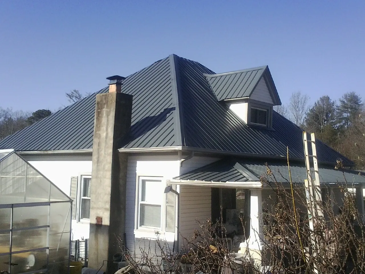 Dark blue standing seam metal roof on a white farmhouse with dormer in Haymarket