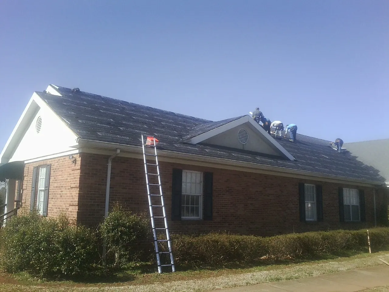 Crew tearing shingles off a brick ranch roof with a ladder set — Metal Roof Repair work by our crew in Haymarket
