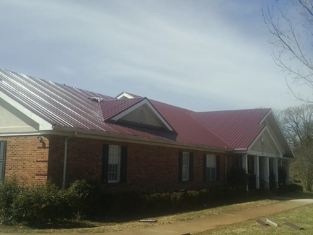 Red metal roof with gabled entries on a long brick building, from a Hail Damage Roof Repair job in Haymarket