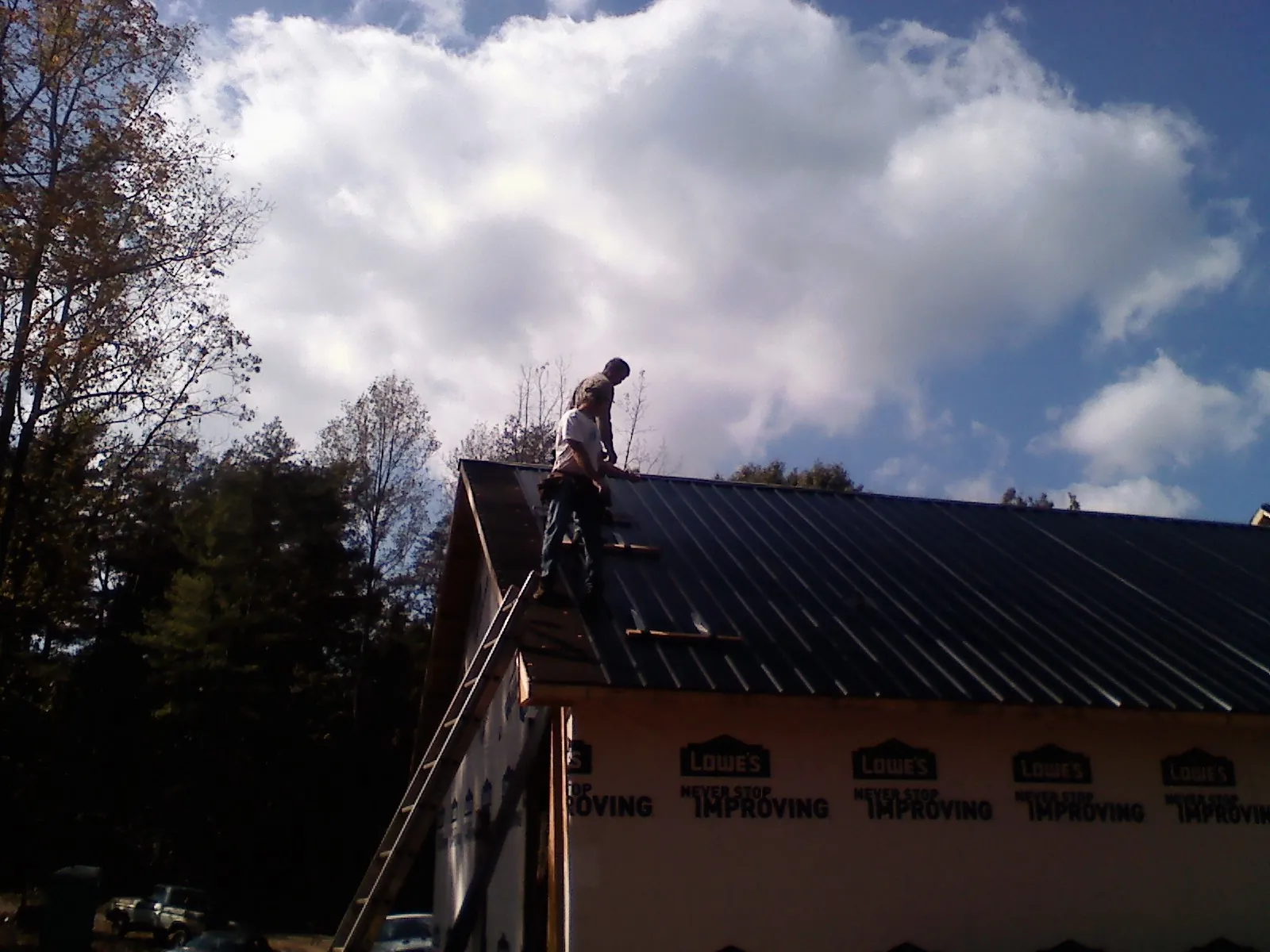 Roofer fastening dark metal panels high against a cloudy sky, from a Roof Inspection job in Haymarket