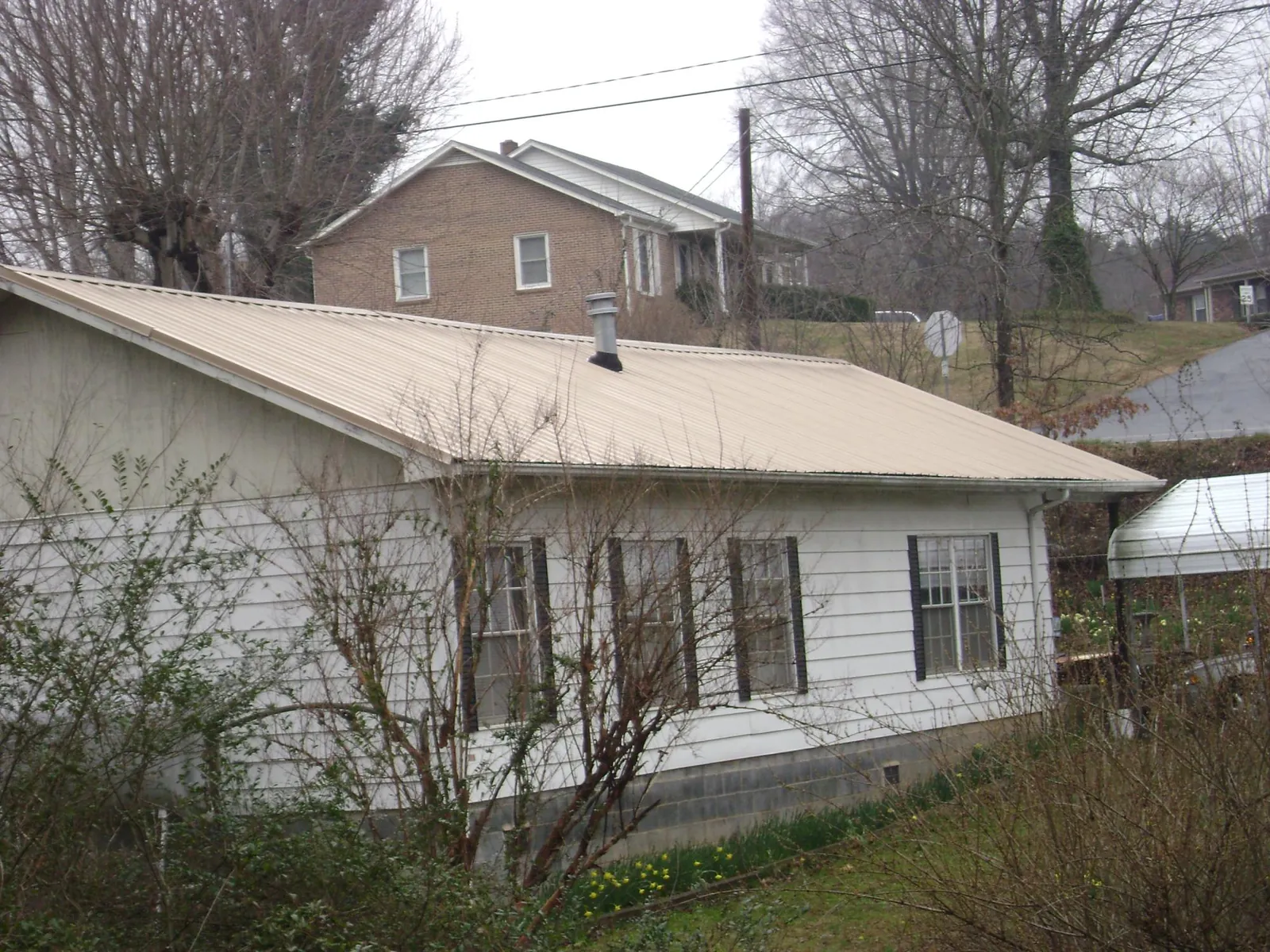 Tan metal roof on a white sided house set into a hillside — Commercial Roofing by Roofing Brothers in Haymarket